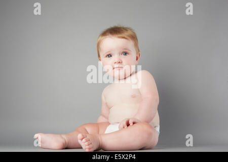 Studio portrait of baby girl sitting up perplexe Banque D'Images