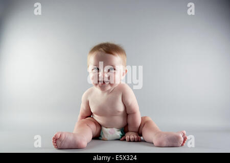 Studio portrait of smiling baby girl sitting up Banque D'Images