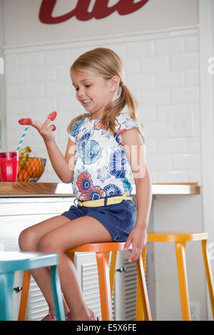 Fille assise sur le tabouret de cuisine avec des framboises sur ses doigts Banque D'Images