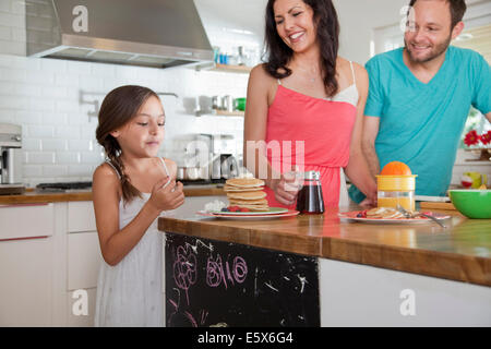 Young parents tentant de fille avec des crêpes au petit déjeuner bar Banque D'Images