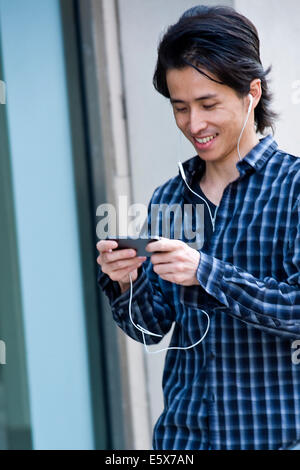 Mid adult man walking down street ville sélection de musique sur smartphone Banque D'Images