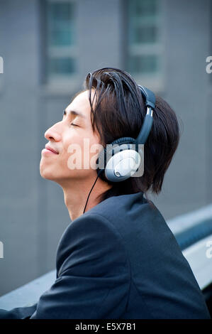 Mid adult businessman on city rooftop listening to music on headphones Banque D'Images
