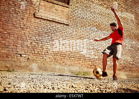 Jeune homme jouant au football sur wasteland Banque D'Images