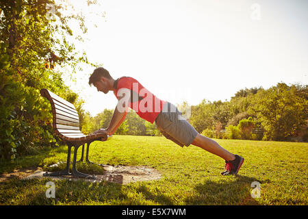 Young male runner faire poussez se lève sur banc de parc Banque D'Images