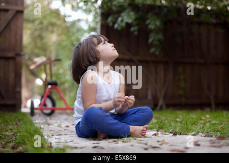 Quatre ans, fille, assis sur chemin de jardin le regard vers le haut Banque D'Images