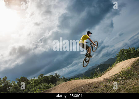 Jeune homme mountain biker jumping mid air on rural pompe voie Banque D'Images
