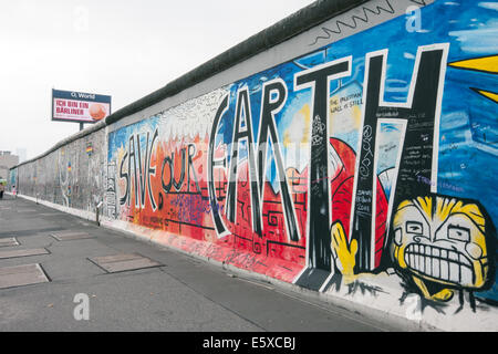 'Save notre terre" artwork sur mur de Berlin, à l'East Side Gallery, sous un écran publicitaire de l'O2 Banque D'Images