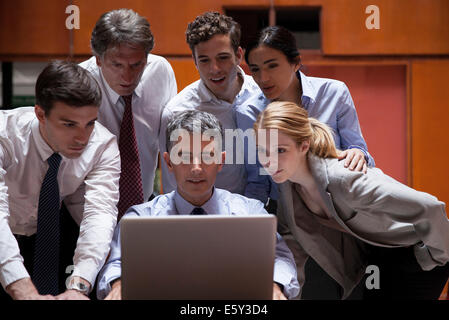 Des collègues de foule autour de collègue regardant par-dessus son épaule at laptop computer Banque D'Images