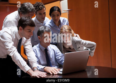 Des collègues de foule autour de collègue regardant par-dessus son épaule at laptop computer Banque D'Images