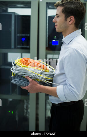 Technicien en informatique transportant des bobines de câbles réseau en salle serveur Banque D'Images