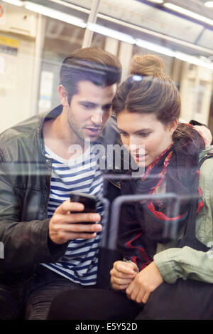 Jeune couple riding subway looking at digital tablet together Banque D'Images