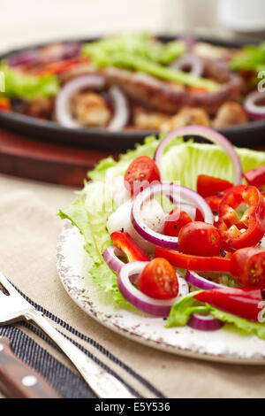 Dés de poulet cuit et saucisse avec oignons, poivrons, mushrrooms et une salade de tomates, champignons, poivrons et la laitue. Banque D'Images