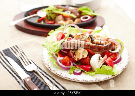 Dés de poulet cuit et saucisse avec oignons, poivrons, mushrrooms et une salade de tomates, champignons, poivrons et la laitue. Banque D'Images