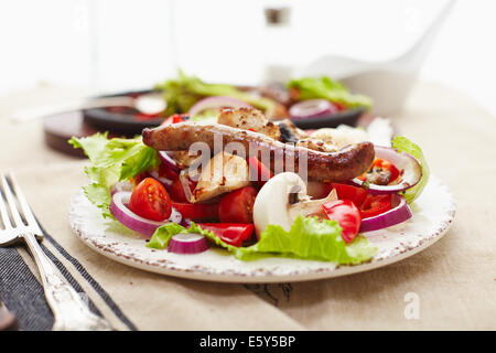 Dés de poulet cuit et saucisse avec oignons, poivrons, mushrrooms et une salade de tomates, champignons, poivrons et la laitue. Banque D'Images