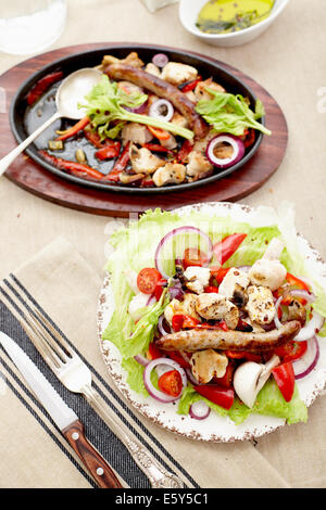 Dés de poulet cuit et saucisse avec oignons, poivrons, mushrrooms et une salade de tomates, champignons, poivrons et la laitue. Banque D'Images