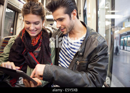 Jeune couple riding subway looking at digital tablet together Banque D'Images