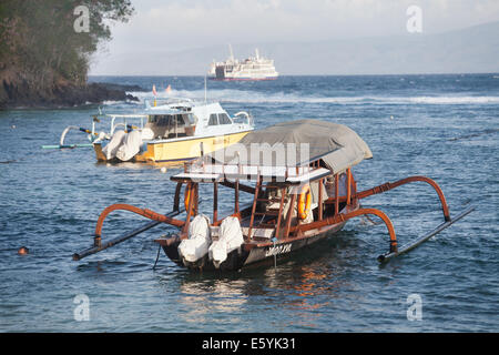 Bateaux amarrés dans la mer sur la côte de bali avec ferry dans la distance à l'horizon de faire son chemin au-dessus de l'eau bateau jukung traditionnel. Banque D'Images