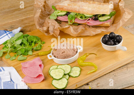 Baguette méditerranéen avec des ingrédients sur planche à découper en bois Banque D'Images