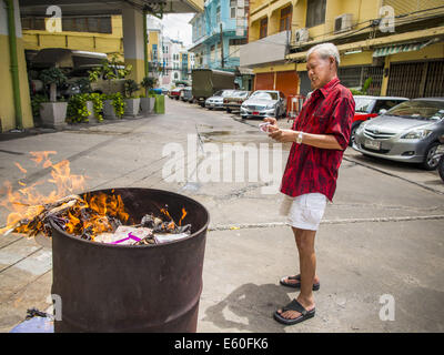 Bangkok, Thaïlande. 10e Août, 2014. Un homme pas en arrière après avoir laissé tomber un tas de ''l'enfer de l'argent'' dans un baril de brûlage à Bangkok pour Ghost Month. L'enfer de l'argent est une forme de joss le papier imprimé pour ressembler à cours légal des billets de banque et est utilisé dans des cérémonies religieuses dans les communautés chinoises. Le septième mois de l'année lunaire chinoise est appelée ''Ghost'' mois pendant lequel les fantômes et les esprits, y compris ceux de l'ancêtres décédés, sortent de la sphère inférieure. Il est courant pour les Chinois de faire mérite au cours du mois par la combustion de ''l'enfer de l'argent'' et la présentation de la nourriture pour les fantômes. (Crédit Banque D'Images
