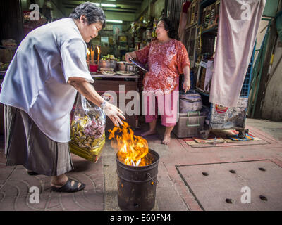 Bangkok, Thaïlande. 10e Août, 2014. Une femme burns joss papier et l'enfer de l'argent sur le premier jour de mois Ghost dans une ruelle dans le quartier chinois de Bangkok. Le septième mois de l'année lunaire chinoise est appelée ''Ghost'' mois pendant lequel les fantômes et les esprits, y compris ceux de l'ancêtres décédés, sortent de la sphère inférieure. Il est courant pour les Chinois de faire mérite au cours du mois par la combustion de ''l'enfer de l'argent'' et la présentation de la nourriture pour les fantômes. Crédit : Jack Kurtz/ZUMA/Alamy Fil Live News Banque D'Images