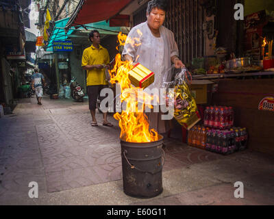 Bangkok, Thaïlande. 10e Août, 2014. Une femme burns joss papier et l'enfer de l'argent sur le premier jour de mois Ghost dans une ruelle dans le quartier chinois de Bangkok. Le septième mois de l'année lunaire chinoise est appelée ''Ghost'' mois pendant lequel les fantômes et les esprits, y compris ceux de l'ancêtres décédés, sortent de la sphère inférieure. Il est courant pour les Chinois de faire mérite au cours du mois par la combustion de ''l'enfer de l'argent'' et la présentation de la nourriture pour les fantômes. Crédit : Jack Kurtz/ZUMA/Alamy Fil Live News Banque D'Images