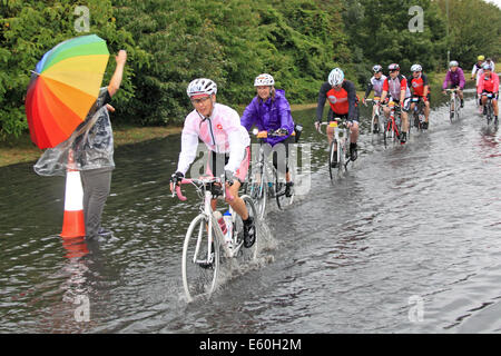 Dimanche 10 août 2014. Dunmurry, Surrey, UK. Les cyclistes la charrue par une route inondée après des pluies torrentielles ont occasionné par les restes de l'ouragan Bertha hits Prudential RideLondon-Surrey 100. 24 000 cyclistes amateurs ont pris part à l'événement qui s'étend sur 100 kilomètres et surtout suit l'itinéraire utilisé dans la course sur route olympique de Londres 2012. Cependant, en raison du mauvais temps, la route a été raccourcie à 86km). Crédit : Ian bouteille/Alamy Live News Banque D'Images