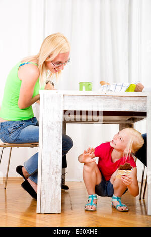 Girl eating chocolate sous table tandis que la famille est le petit-déjeuner Banque D'Images