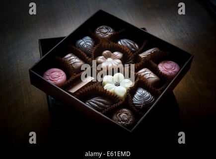 Une boîte carrée de couleur assortis chocolats en forme et reposant sur une table en bois Banque D'Images