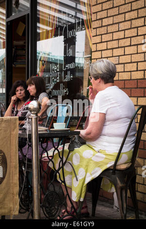 Senior, dame aux cheveux gris, assis dehors dans un café avec une tasse de café et de tabac. Banque D'Images