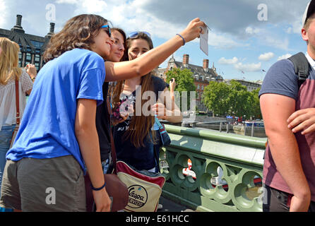 Londres, Angleterre, Royaume-Uni. Trois jeunes femmes sur le pont de Westminster en tenant un téléphone mobile avec un selfies Banque D'Images