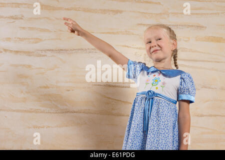 Jolie petite fille blonde avec ses cheveux en amorces pointant vers le haut avec un sourire heureux, low angle view contre un mur avec copyspace. Banque D'Images