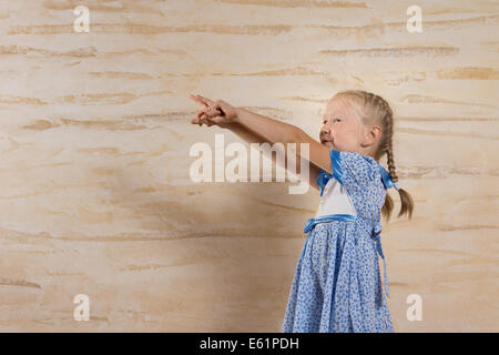 Jolie petite fille blonde avec ses cheveux en amorces pointant avec deux mains à gauche de l'armature et copyspace Banque D'Images