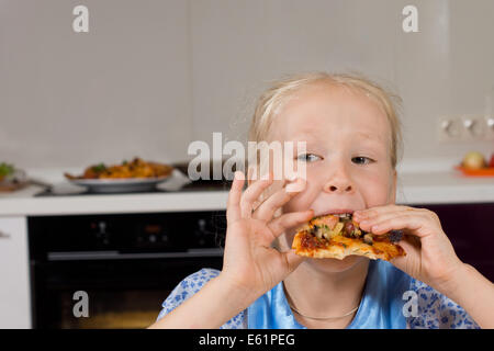 Jeune fille en prenant une bouchée de pizza italienne maison d'oeil sur le côté alors qu'elle apprécie son repas avec avidité Banque D'Images