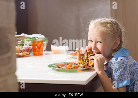 Jolie petite fille avide de dévorer des pizzas jusqu'à de prendre une bouchée avec un sourire espiègle de jouissance Banque D'Images