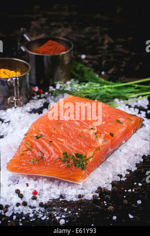 Morceau de saumon salé, servi avec de l'aneth et les épices sur le sel de mer sur table en bois noir Banque D'Images