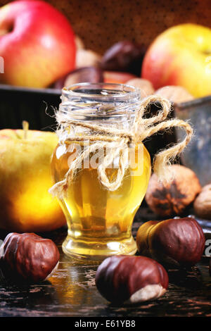 Pot de miel en verre avec les pommes, les châtaignes et les noix de table en bois noir Banque D'Images