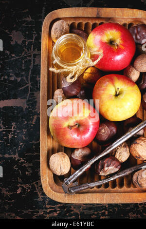 Pot de miel en verre avec les pommes, les châtaignes et les noix dans la plaque de bois sur table en bois noir. Vue d'en haut Banque D'Images