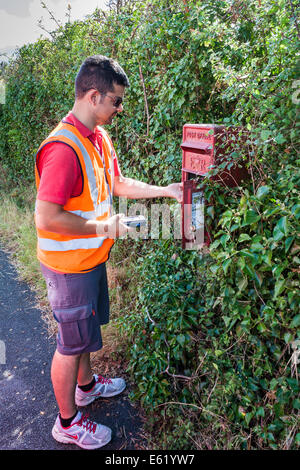 Royal Mail postman recueille des messages de pilier rural fort Banque D'Images