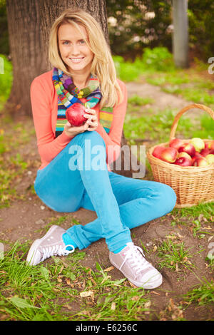 Jolie fille avec pomme rouge assis sur la masse dans park Banque D'Images