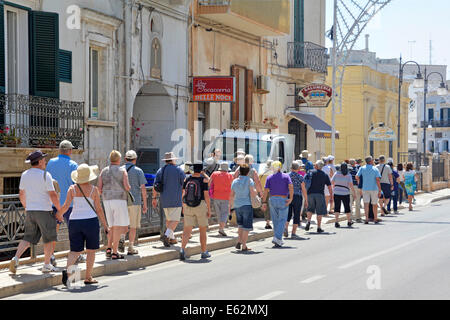 Vue arrière groupe touristes de vacances les gens de visite groupe en car partie marchant dans la ligne sur la rue dans la province de Polignano a Mare de Bari Apulia Puglia Italie Banque D'Images