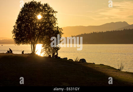 Coucher de soleil sur Burrard Inlet avec eau et montagnes, silhouettes d'arbres et de personnes au parc marin Barnett, Burnaby, Colombie-Britannique, Canada Banque D'Images