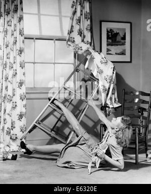 Années 1940 Années 1950 FEMME LA CHUTE D'ESCABEAU SUSPENDU RIDEAUX DE FENÊTRE Banque D'Images