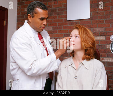 Années 1990, African American MAN OPTOMÉTRISTE METTANT EN LENTILLES DE CONTACT CAUCASIAN WOMAN'S EYE Banque D'Images