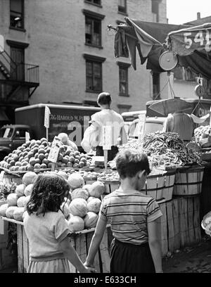 1950 JEUNE FILLE ANONYME ET BOY HOLDING HANDS EN PASSANT DEVANT PRODUIRE EN DÉCROCHAGE DU MARCHÉ ALIMENTAIRE urbaine de Philadelphie, en Pennsylvanie, USA Banque D'Images