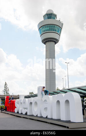 La tour de contrôle de l'aéroport de Schiphol blanc contre ciel nuageux avec le JE SUIS Amsterdam signe de l'arrivée/de départ pont en avant. Banque D'Images