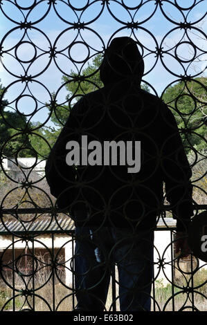 Hooded man looking at vue du balcon d'une maison abandonnée et vintage porte de fer motif cercles. Banque D'Images