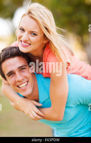 Cheerful young woman piggyback ride on boyfriends back outdoors Banque D'Images