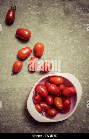 Petites tomates cerise s'échappant d'un bol. Moody la photographie culinaire. Banque D'Images