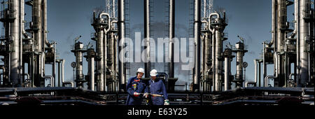 Deux travailleurs-huile debout devant des grands de l'industrie de la raffinerie Banque D'Images