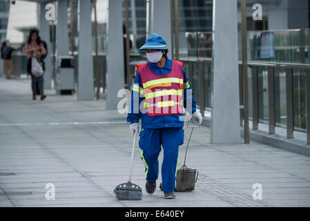Nettoyant de la rue de sexe féminin portant un gilet de sécurité, masque et la tenue d'un outil de balayage, Shanghai, Chine Banque D'Images